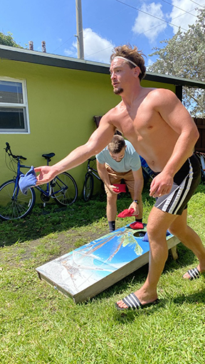 Men playing cornhole in a sunny Delray Beach backyard sober living house, showing brotherhood and fun in sobriety